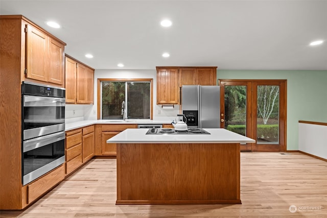 kitchen with stainless steel appliances, a center island, sink, and light hardwood / wood-style flooring