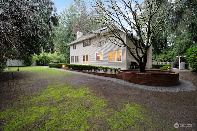 view of front of home featuring driveway, a chimney, and fence