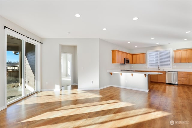 kitchen with appliances with stainless steel finishes, a breakfast bar area, and light hardwood / wood-style flooring