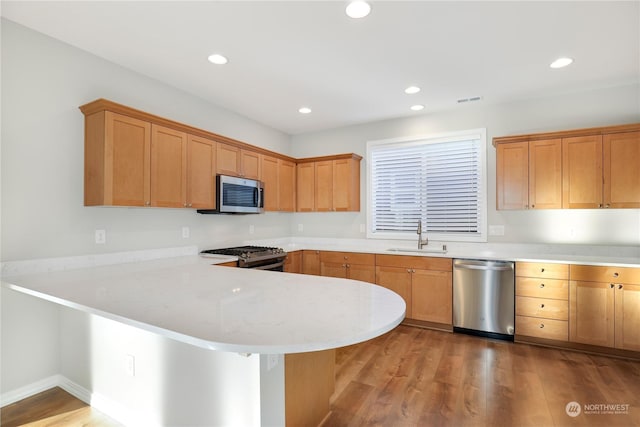 kitchen with sink, light wood-type flooring, kitchen peninsula, stainless steel appliances, and light stone countertops