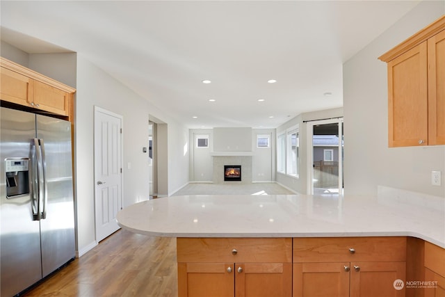 kitchen featuring stainless steel fridge with ice dispenser, a fireplace, light stone counters, kitchen peninsula, and light hardwood / wood-style flooring