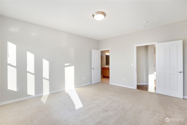 unfurnished bedroom with ensuite bath and light colored carpet