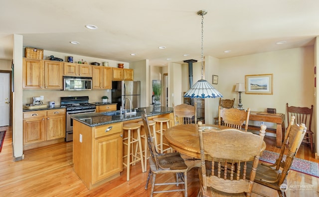 kitchen featuring pendant lighting, sink, a kitchen island with sink, stainless steel appliances, and light wood-type flooring