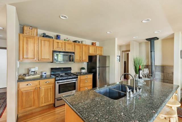 kitchen featuring sink, appliances with stainless steel finishes, dark stone countertops, light hardwood / wood-style floors, and a kitchen bar