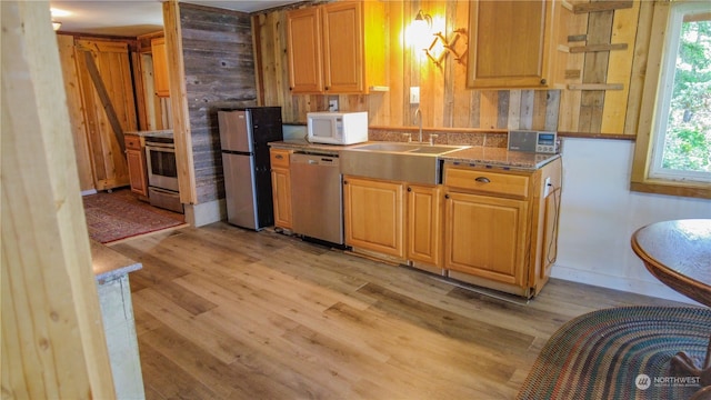 kitchen with appliances with stainless steel finishes, sink, light wood-type flooring, and wood walls