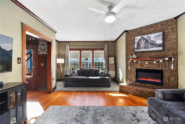 living room featuring hardwood / wood-style flooring, crown molding, a stone fireplace, and ceiling fan