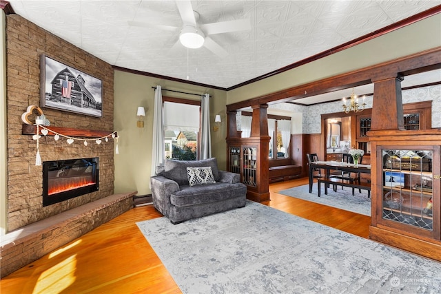 living room with crown molding, a stone fireplace, wood-type flooring, and an inviting chandelier