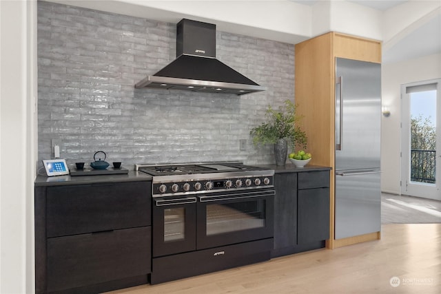 kitchen featuring tasteful backsplash, premium appliances, light hardwood / wood-style floors, and wall chimney exhaust hood