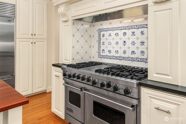 kitchen with high end appliances, backsplash, ventilation hood, and light wood-type flooring