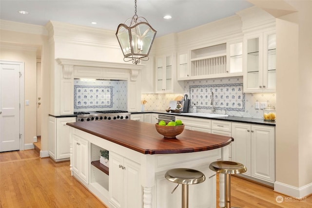 kitchen featuring pendant lighting, butcher block countertops, sink, white cabinetry, and a center island