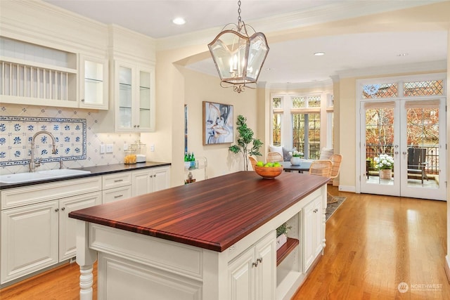 kitchen with butcher block counters, sink, white cabinetry, hanging light fixtures, and decorative backsplash