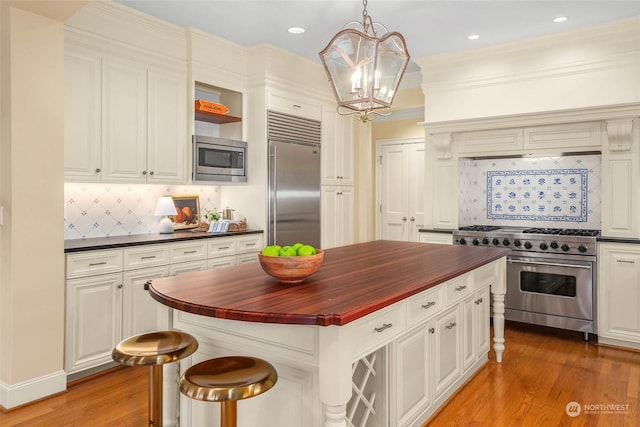 kitchen featuring pendant lighting, tasteful backsplash, wooden counters, a kitchen bar, and built in appliances