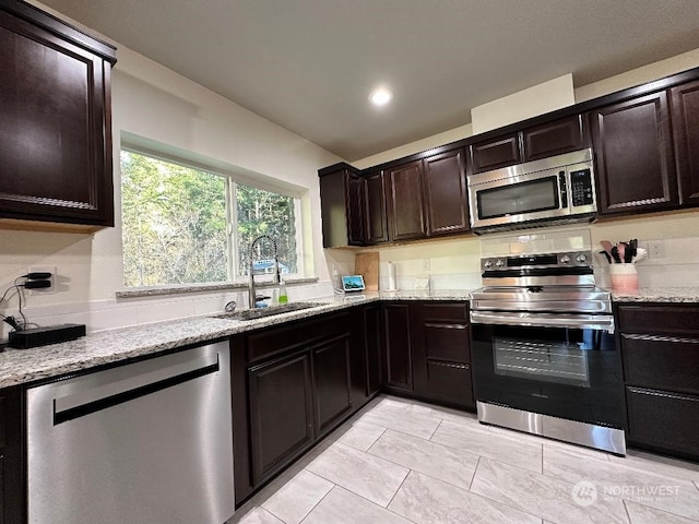 kitchen with light stone counters, dark brown cabinetry, stainless steel appliances, and sink