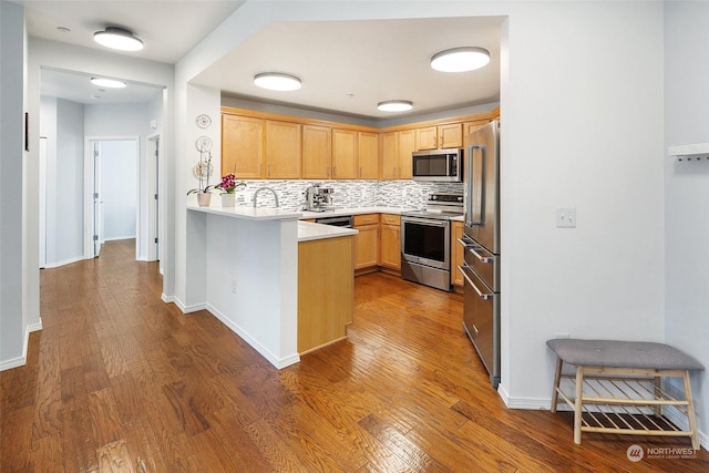 kitchen with backsplash, hardwood / wood-style floors, stainless steel appliances, light brown cabinetry, and kitchen peninsula