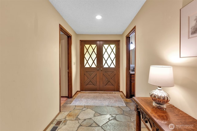 entryway with a textured ceiling, visible vents, baseboards, french doors, and stone tile flooring