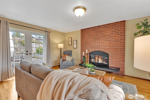 living area with light wood-type flooring, a brick fireplace, and french doors