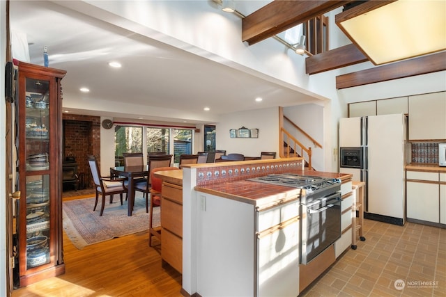 kitchen with white cabinetry, white refrigerator with ice dispenser, beamed ceiling, and stainless steel gas range