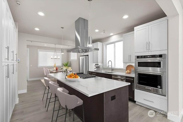 kitchen with sink, white cabinetry, island range hood, appliances with stainless steel finishes, and a kitchen island