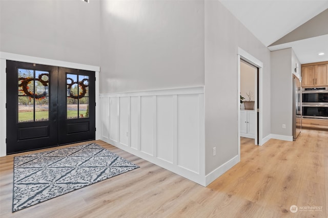 entryway with light hardwood / wood-style flooring, french doors, and vaulted ceiling