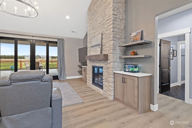 living room featuring french doors, a stone fireplace, an inviting chandelier, high vaulted ceiling, and light hardwood / wood-style floors