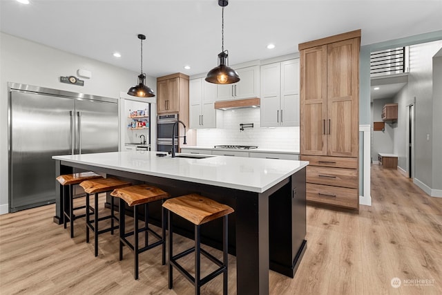 kitchen with hanging light fixtures, stainless steel built in refrigerator, gas stovetop, white cabinets, and a center island with sink