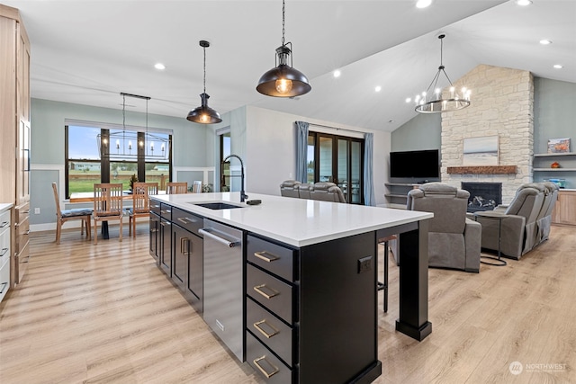 kitchen with light hardwood / wood-style flooring, a kitchen island with sink, sink, and decorative light fixtures