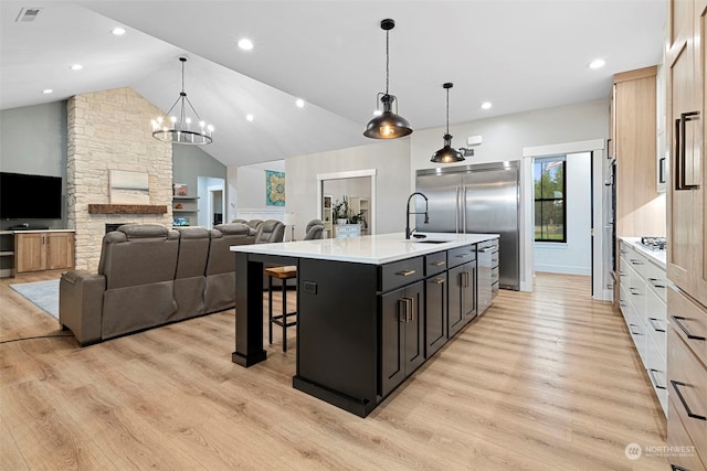 kitchen with built in refrigerator, decorative light fixtures, vaulted ceiling, a center island with sink, and light hardwood / wood-style flooring