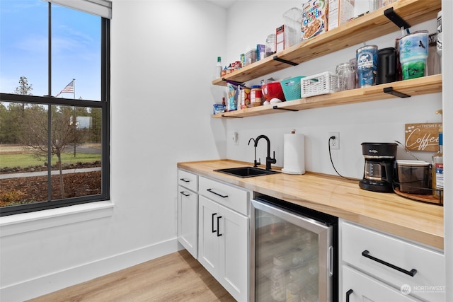 bar with wood counters, sink, white cabinets, beverage cooler, and light hardwood / wood-style flooring