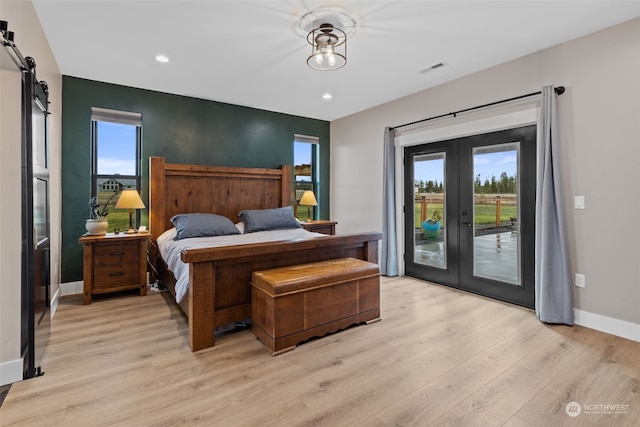 bedroom featuring french doors, access to exterior, light wood-type flooring, a barn door, and multiple windows