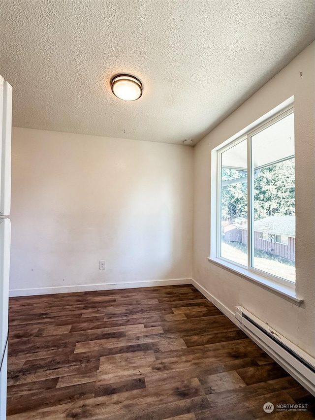 spare room featuring dark wood-type flooring, a baseboard radiator, and a textured ceiling