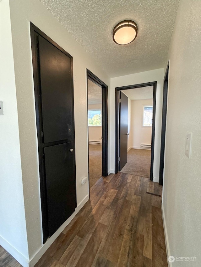 corridor with dark hardwood / wood-style flooring, a textured ceiling, and a baseboard heating unit