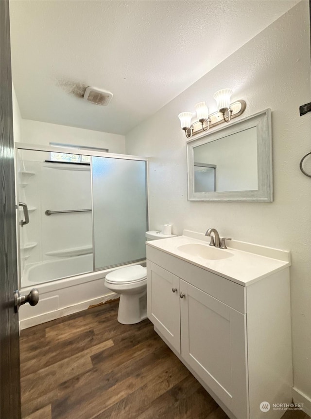 full bathroom with wood-type flooring, enclosed tub / shower combo, vanity, toilet, and a textured ceiling