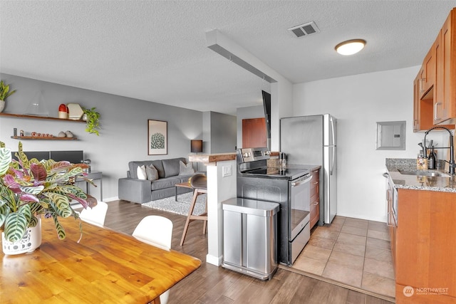 kitchen featuring visible vents, light wood-style flooring, brown cabinetry, stainless steel range with electric cooktop, and a sink