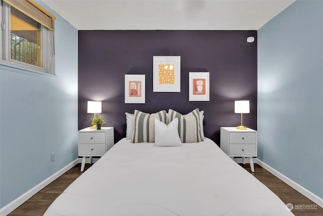 bedroom featuring an accent wall, dark wood finished floors, and baseboards