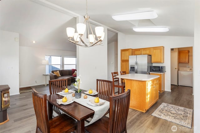 dining area with lofted ceiling, washer / clothes dryer, wood finished floors, a wood stove, and an inviting chandelier