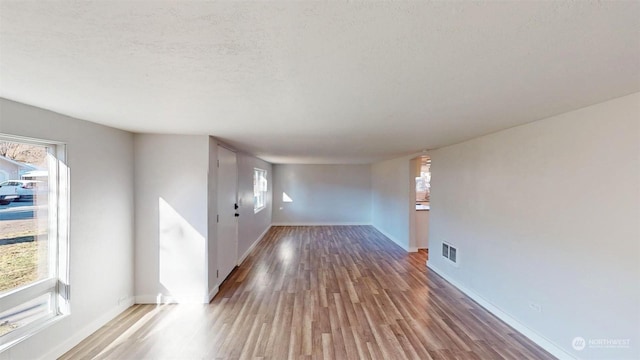 empty room featuring a healthy amount of sunlight, hardwood / wood-style floors, and a textured ceiling