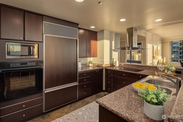 kitchen featuring stone countertops, island range hood, sink, black appliances, and dark brown cabinets