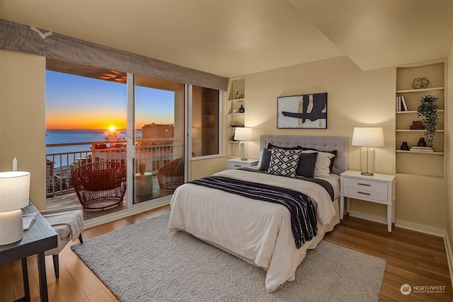 bedroom featuring access to exterior, hardwood / wood-style floors, and a water view