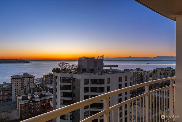 balcony at dusk featuring a water view