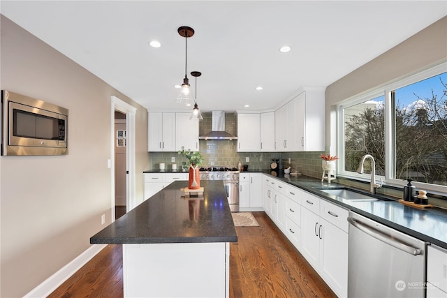 kitchen with appliances with stainless steel finishes, sink, hanging light fixtures, a center island, and wall chimney exhaust hood