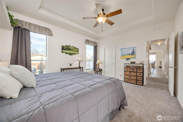 carpeted bedroom with a raised ceiling and ceiling fan