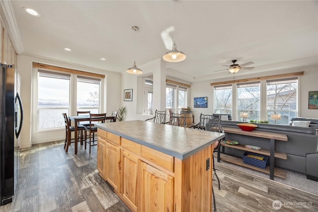 kitchen with a kitchen island, hanging light fixtures, ornamental molding, black fridge, and dark wood-type flooring