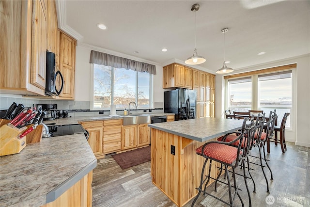 kitchen featuring pendant lighting, sink, ornamental molding, black appliances, and a kitchen island