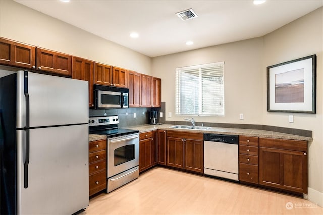 kitchen featuring tasteful backsplash, stainless steel appliances, light hardwood / wood-style floors, and sink