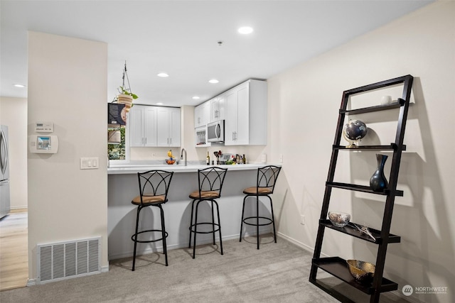 kitchen with white cabinetry, sink, a kitchen breakfast bar, light colored carpet, and kitchen peninsula