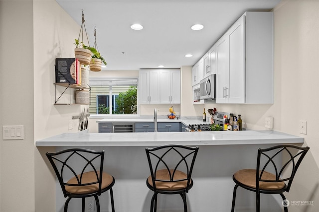 kitchen featuring appliances with stainless steel finishes, white cabinets, a kitchen bar, and kitchen peninsula