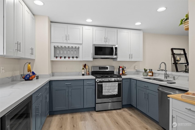 kitchen with sink, appliances with stainless steel finishes, beverage cooler, light hardwood / wood-style floors, and white cabinets