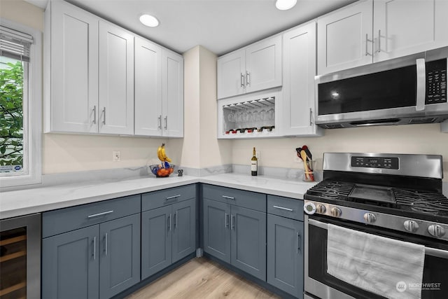 kitchen with wine cooler, appliances with stainless steel finishes, light stone counters, and white cabinets