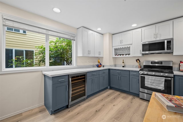 kitchen with gray cabinets, white cabinetry, stainless steel appliances, beverage cooler, and light wood-type flooring