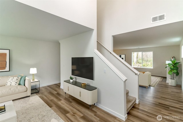 living area featuring a towering ceiling, baseboards, stairs, visible vents, and wood finished floors